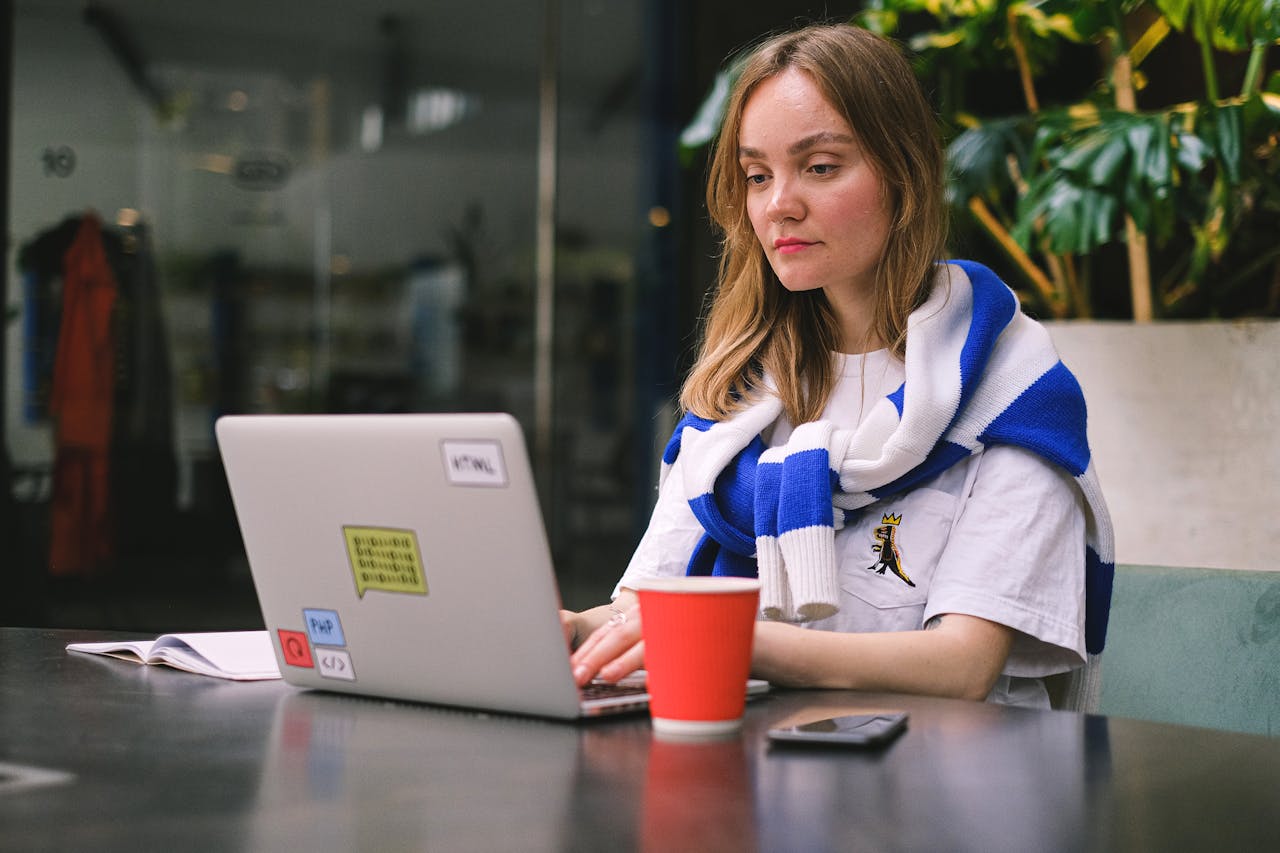 Young woman focused on laptop work in a modern cafe setting, surrounded by technology.